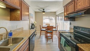 A kitchen with wooden cabinets, a granite countertop, a stainless steel sink, a black stove, and a ceiling fan. - Cozy Fresno Condo w/ Balcony & Pool Access (Fresno)