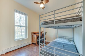 A bunk bed room with a desk and chair, a window, and a ceiling fan.