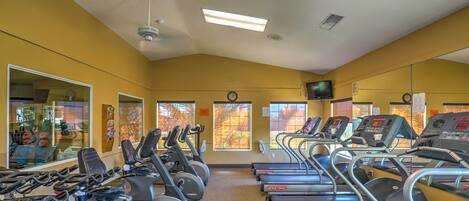 Un gimnasio con varias cintas de correr y bicicletas estáticas, ventanas amplias y un espejo que refleja los equipos.
