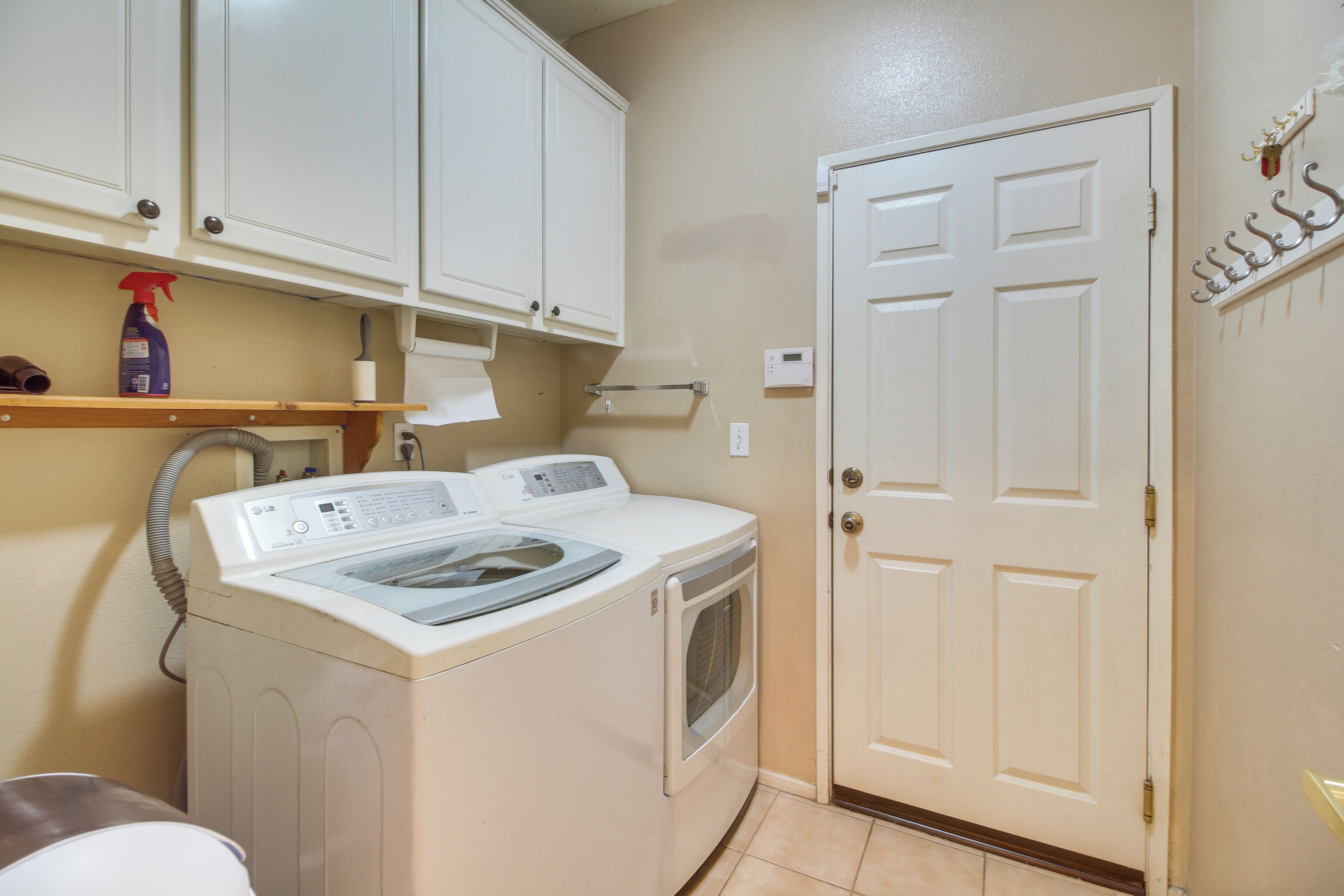 A laundry room with a washer and dryer, a shelf with cleaning supplies, and a door with a coat rack.