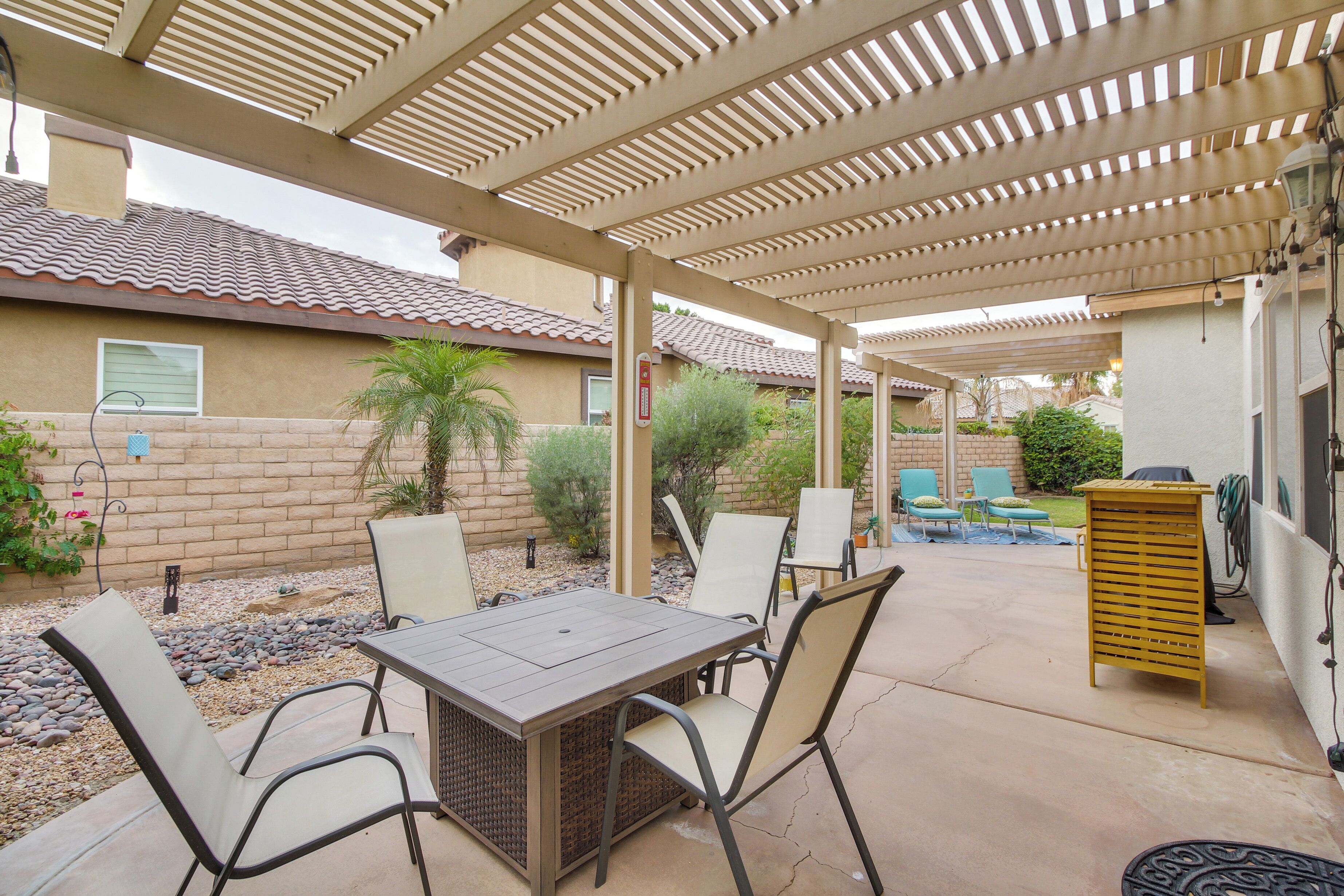 A covered patio area with a table and chairs, a pergola overhead, and a small garden with plants and a patio table.