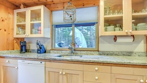A kitchen with wooden cabinets, a built-in dishwasher, and a window with a view of the outdoors. - Charming Tamworth Cabin w/ Grill & Fireplace (Tamworth)