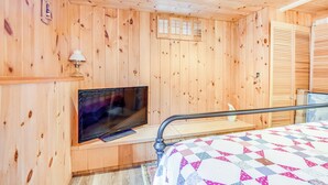 A wooden-paneled room with a bed, a television on a stand, and a small table. - Charming Tamworth Cabin w/ Grill & Fireplace (Tamworth)