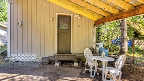 Une cabane en bois avec une véranda, deux chaises blanches, une petite table et une porte avec une fenêtre.