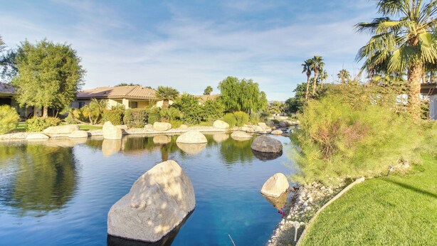 A serene outdoor pool area with large rocks, palm trees, and a clear blue sky. - 2 Mi to Empire Polo Club: Indio Home w/ Fireplace! (Indio)
