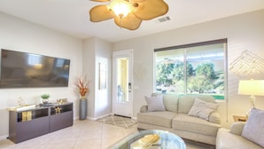 A modern living room with a flat-screen TV, a glass coffee table, a sofa, and a dining area with a cabinet. - 2 Mi to Empire Polo Club: Indio Home w/ Fireplace! (Indio)