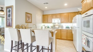 A modern kitchen with wooden cabinets, a white refrigerator, and a bar area with two chairs. - 2 Mi to Empire Polo Club: Indio Home w/ Fireplace! (Indio)