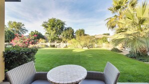A patio with wicker furniture and a round table, surrounded by a well-maintained lawn and various plants. - 2 Mi to Empire Polo Club: Indio Home w/ Fireplace! (Indio)