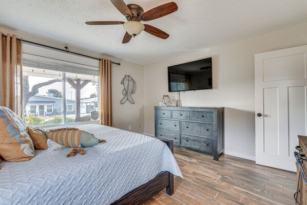 A bedroom with a bed, a ceiling fan, a dresser, a TV, and a window with curtains.