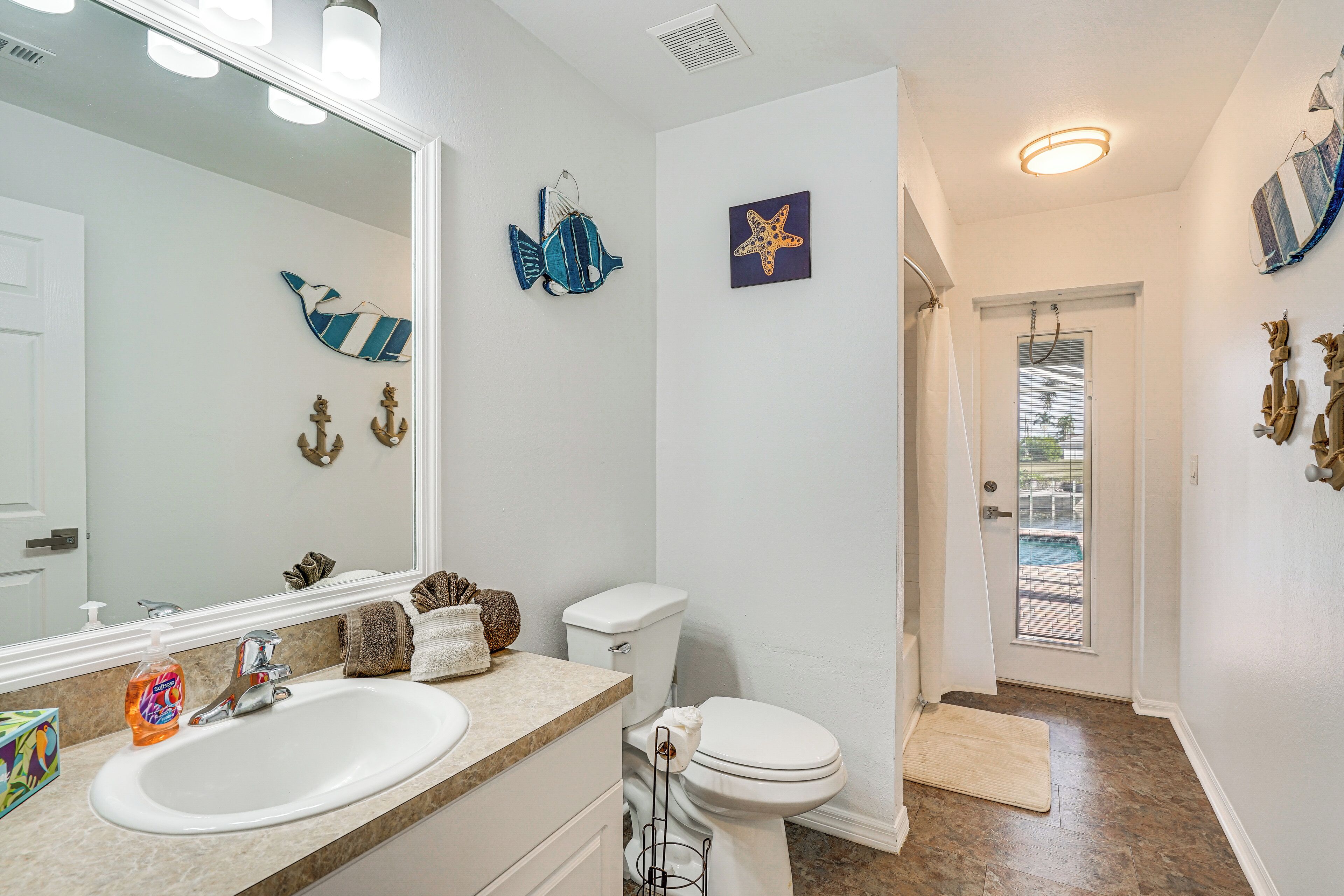 A bathroom with a white sink, a toilet, and a mirror. There are decorative items on the wall, including a starfish and a fish.