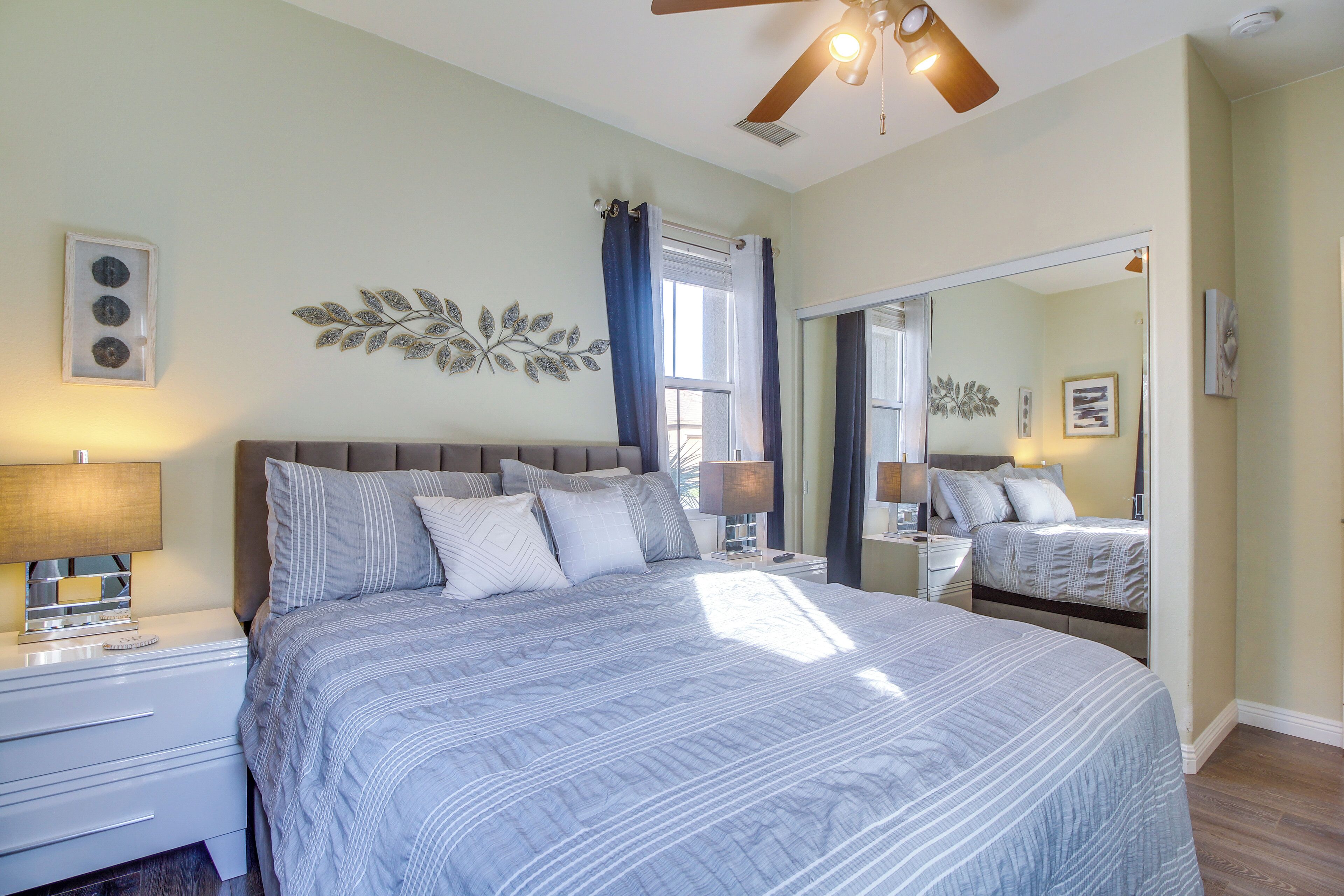 A bedroom with a large bed, two bedside tables, a ceiling fan, and a mirror.