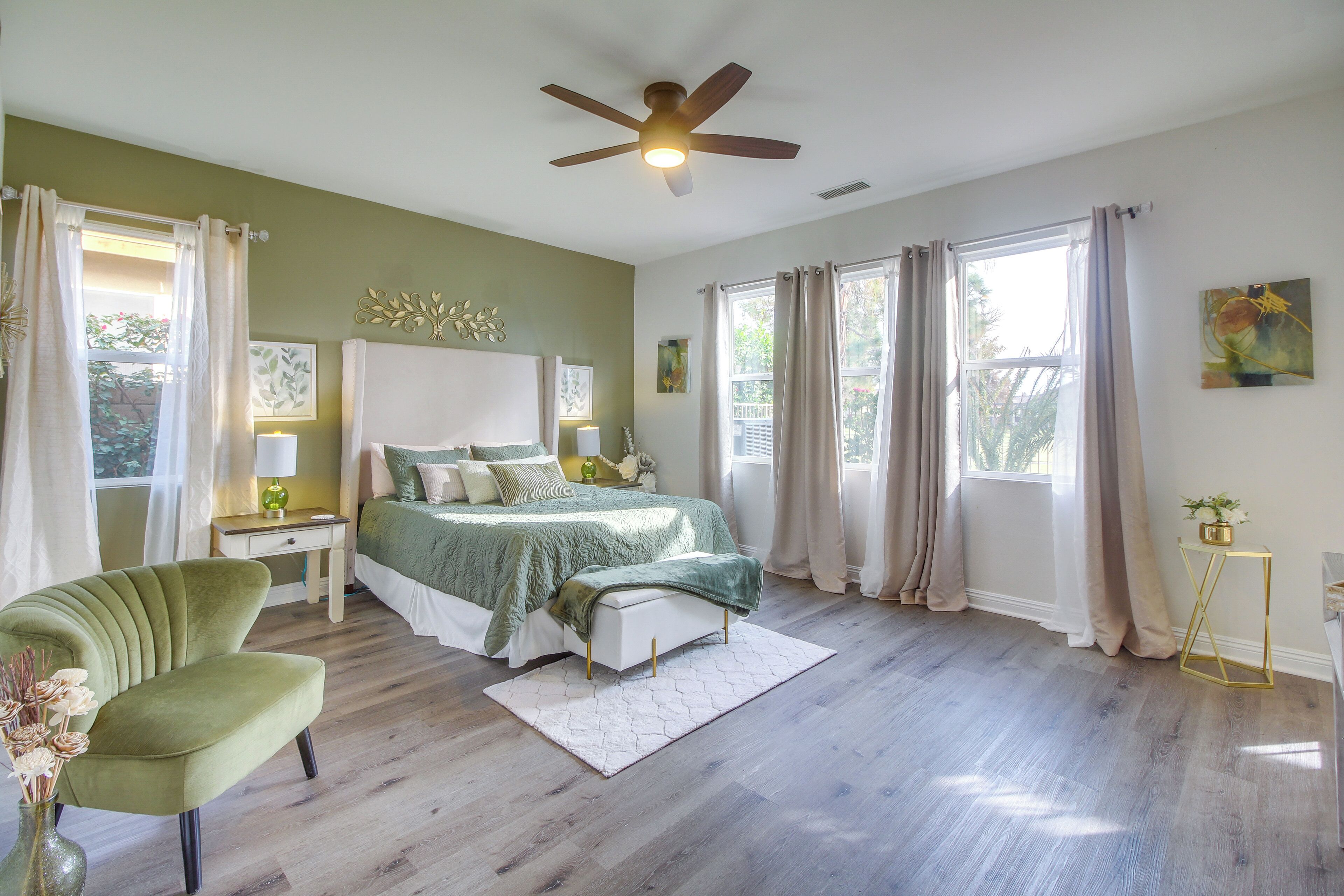 A bedroom with a bed, a green armchair, a bedside table with a lamp, and a ceiling fan.