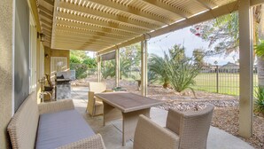 Patio esterno con mobili in vimini, un barbecue e vista su un giardino curato.