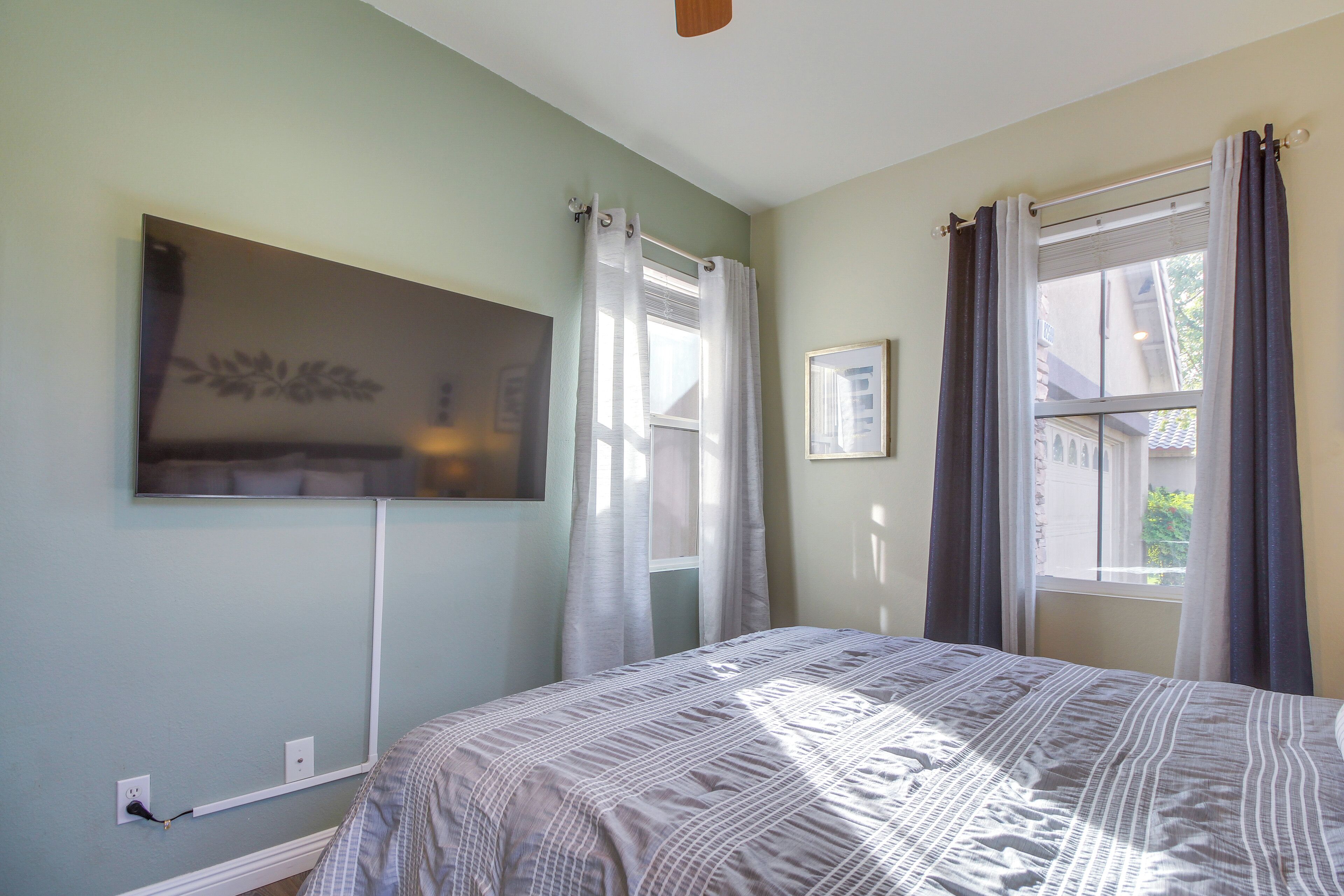 Une chambre à coucher avec un lit, une fen être avec des rideaux, un téléviseur fixé au mur et une prise de courant.