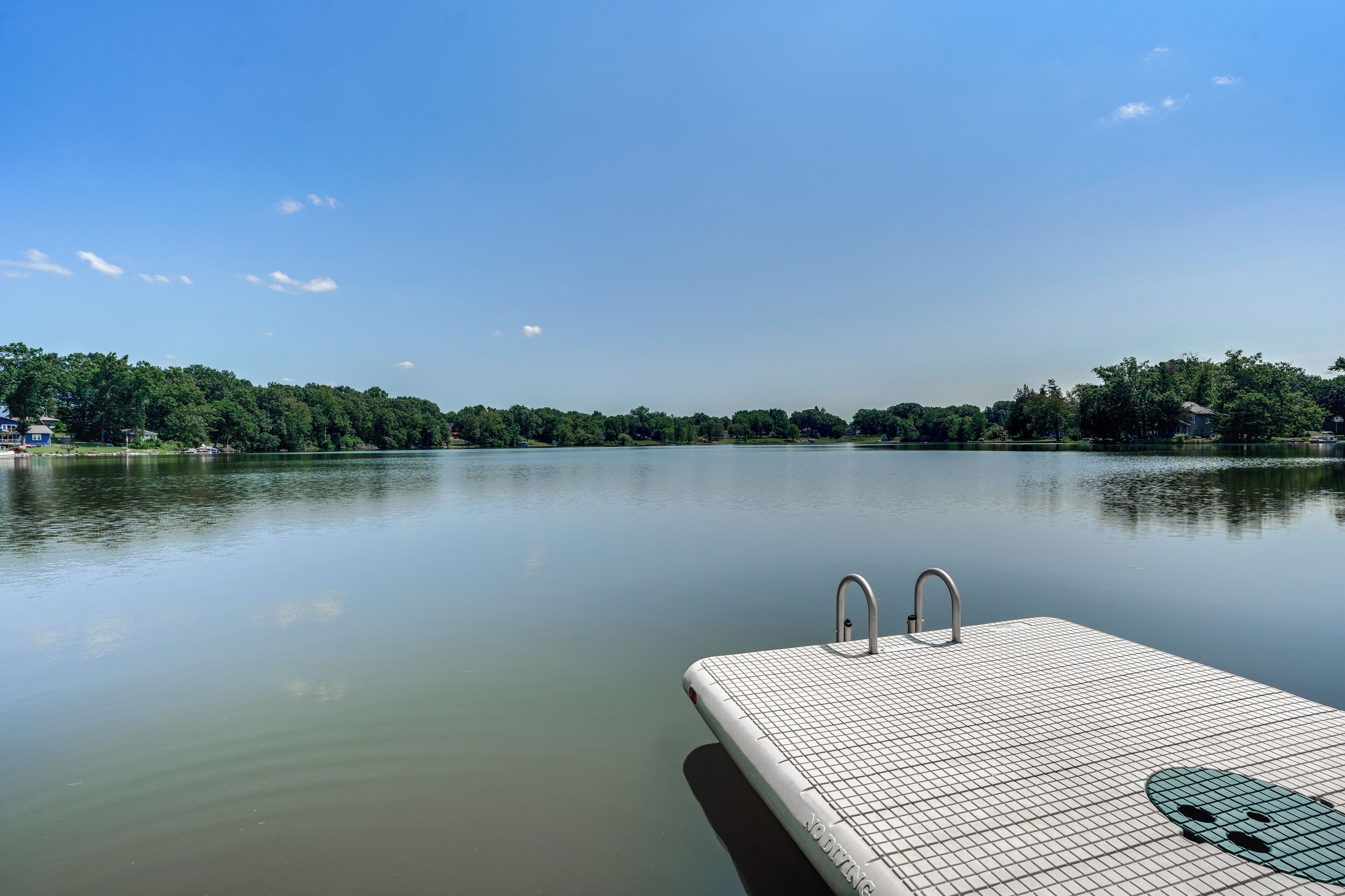 Un lac paisible, avec un ponton flottant et un ciel dégagé.