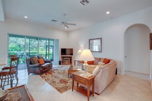 A spacious living room with a large window, a ceiling fan, a flat-screen TV, and a sofa set. - Fort Myers Vacation Rental w/ Pool Access! (Fort Myers)