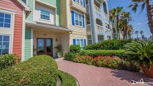 A multi-story hotel with colorful exterior walls, a brick pathway, and well-maintained landscaping. - Gulf & Pool view, Washer & Dryer, Families Love it (Galveston)