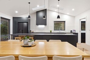A modern kitchen with dark cabinets, a wooden dining table, and pendant lights.