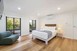 A modern bedroom with a large bed, two bedside lamps, a green armchair, and a sliding glass door leading to a balcony.