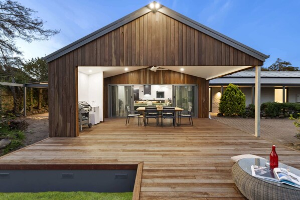 A modern house with a wooden exterior, a covered patio with a dining area, and a swimming pool.
