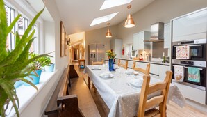 Eine moderne Küche mit Essbereich, mit einem langen Tisch, gedeckt für vier Personen, einem eingebauten Backofen und einem Oberlicht über der Küche.