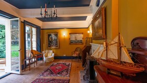 Ein Zimmer mit großem Fenster, einer Kristalllüster, einem hölzernen Schiffmodell und einem Gemälde an der Wand.