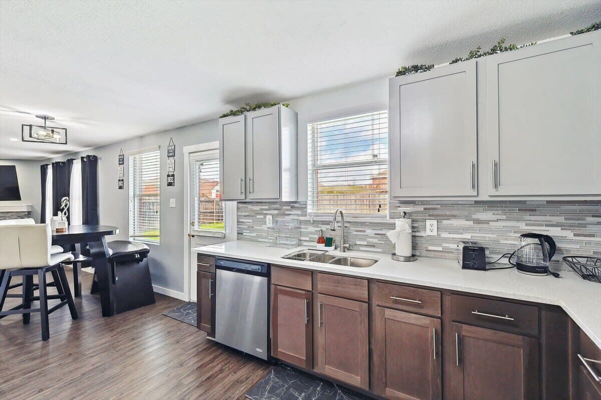 A modern kitchen with grey cabinets, a dishwasher, a coffee maker, and a window with blinds.
