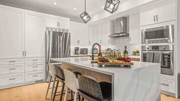 A modern kitchen with white cabinets, stainless steel appliances, and a marble island with bar stools.
