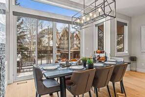A dining area with a large table set for four, large windows offering a view of a snowy landscape and buildings.