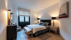 A bedroom with a bed, bedside tables, a bench, a dresser, and a window with a radiator. - Luxurious apartment in the heart of Annecy (Annecy)