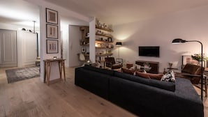 A modern living room with a dark sofa, wooden shelves, a flat-screen TV, and a lamp. - Luxurious apartment in the heart of Annecy (Annecy)