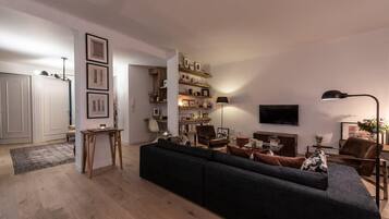 Un salon moderne avec un canapé foncé, des étagères en bois, un téléviseur à écran plat et une lampe.
