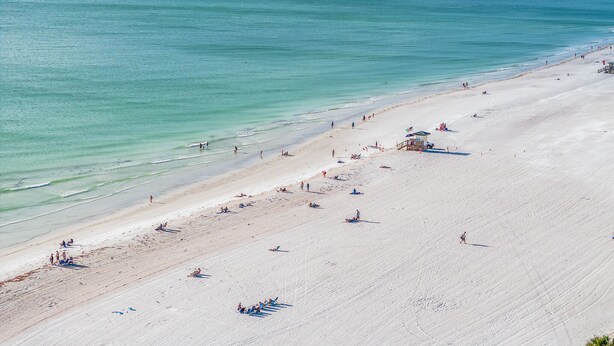 A wide beach with clear turquoise water and a sandy shore.
