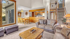 A spacious living room with a leather sofa, a wooden coffee table, and a dining area with wooden chairs. - Wood fireplace, Wi-Fi access, guest perks, seasonal pool, tennis courts and hot tub access (Sunriver)