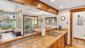 A kitchen with a large island, wooden cabinets, a sink, and a dining area with chairs. - Wood fireplace, Wi-Fi access, guest perks, seasonal pool, tennis courts and hot tub access (Sunriver)