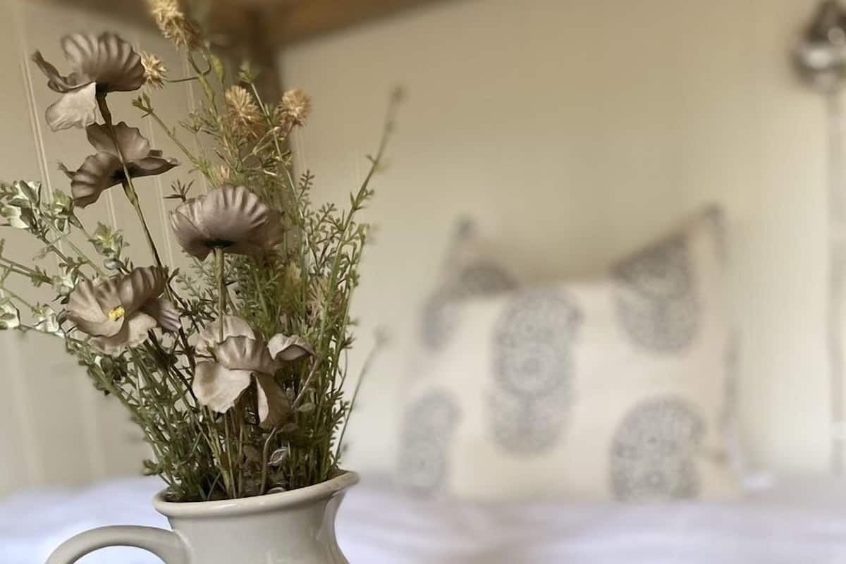 A room with a bed, a decorative vase with dried flowers, and a tray with blue cups.