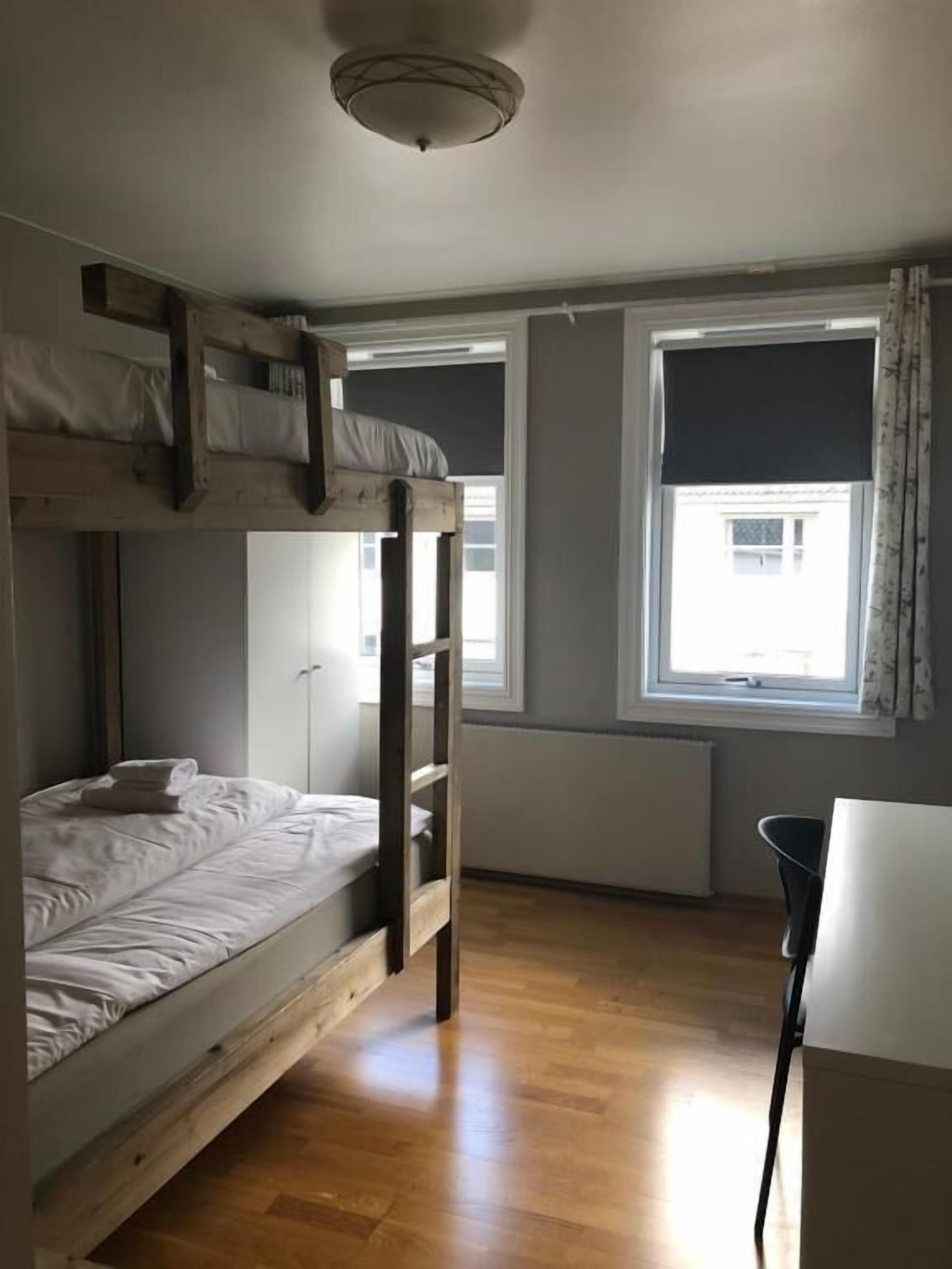 Habitación con literas, escritorio, silla, radiador y ventana con cortinas.