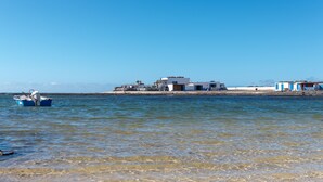 A coastal area with a small boat near the shore, a row of buildings with blue and white exteriors, and a clear blue sky.