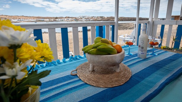 A beachside table with a woven placemat, a bowl of fruit, and a bottle of water.