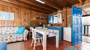 A cozy cabin interior with a wooden interior, a dining table with a blue tablecloth, a sofa with a floral pattern, and a kitchen area with a blue door.