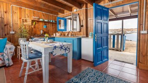 A wooden cabin with a dining area, kitchen, and a view of the beach.