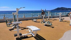 Area fitness all'aperto con attrezzature per esercizi, una persona che si allena e vista sul mare e un'isola in lontananza.