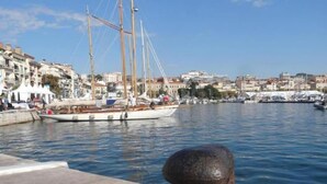 Un porto con una barca a vela ormeggiata, un molo in pietra e uno skyline sullo sfondo.