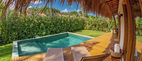A wooden deck with a pool, lounge chairs, and a thatched roof structure.