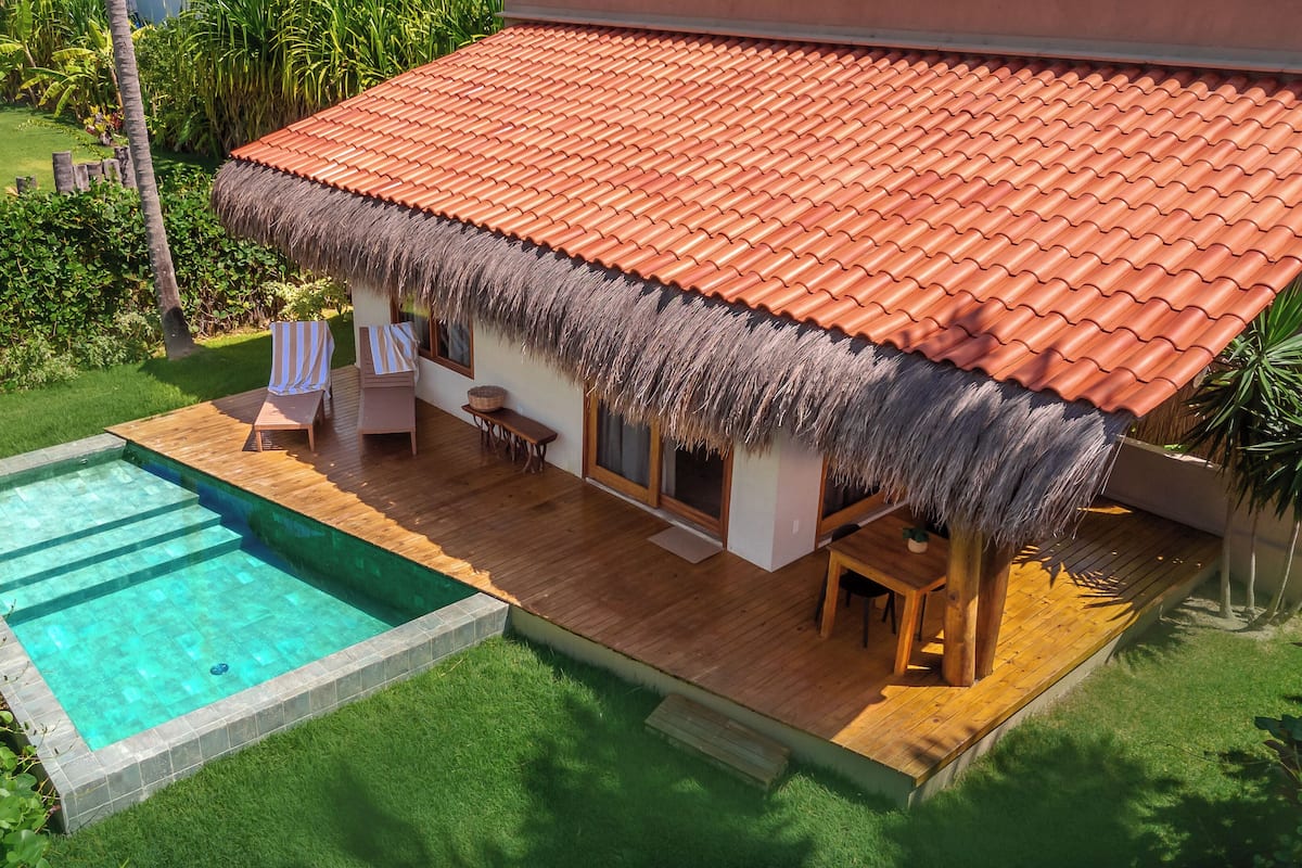 A house with a red tiled roof, a thatched roof over the porch, a swimming pool, and a wooden deck.