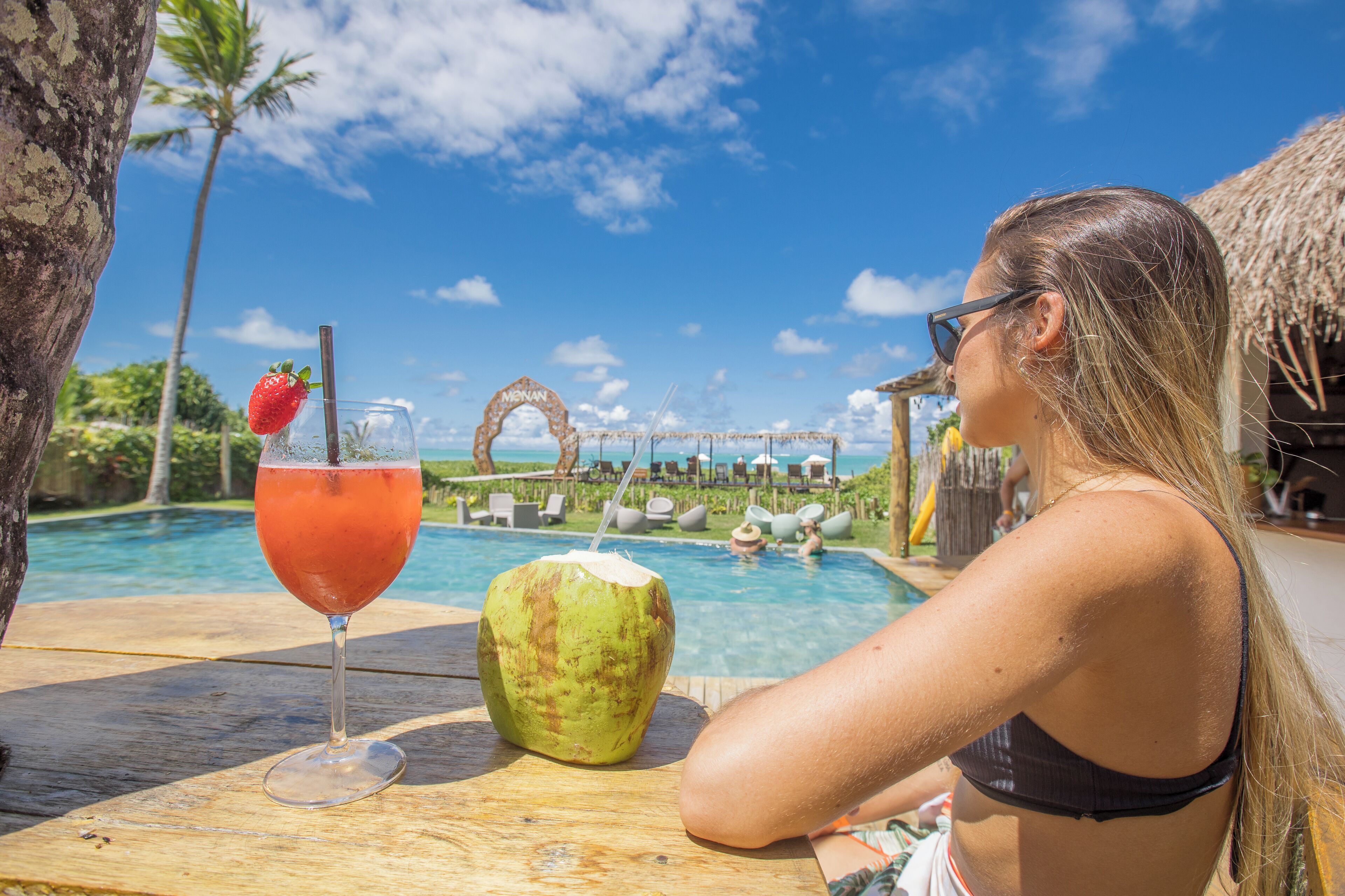 Vista de la piscina con una bebida, un coco y un entorno tropical.