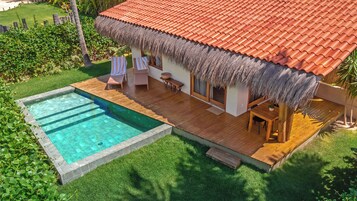 Una casa con piscina, terraza de madera y techo de paja.