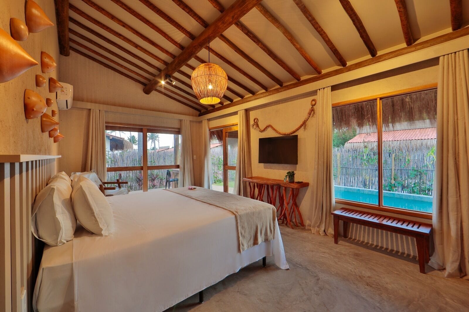 Een ruime slaapkamer met een groot bed, een houten plafond, een televisie en uitzicht op een zwembad.