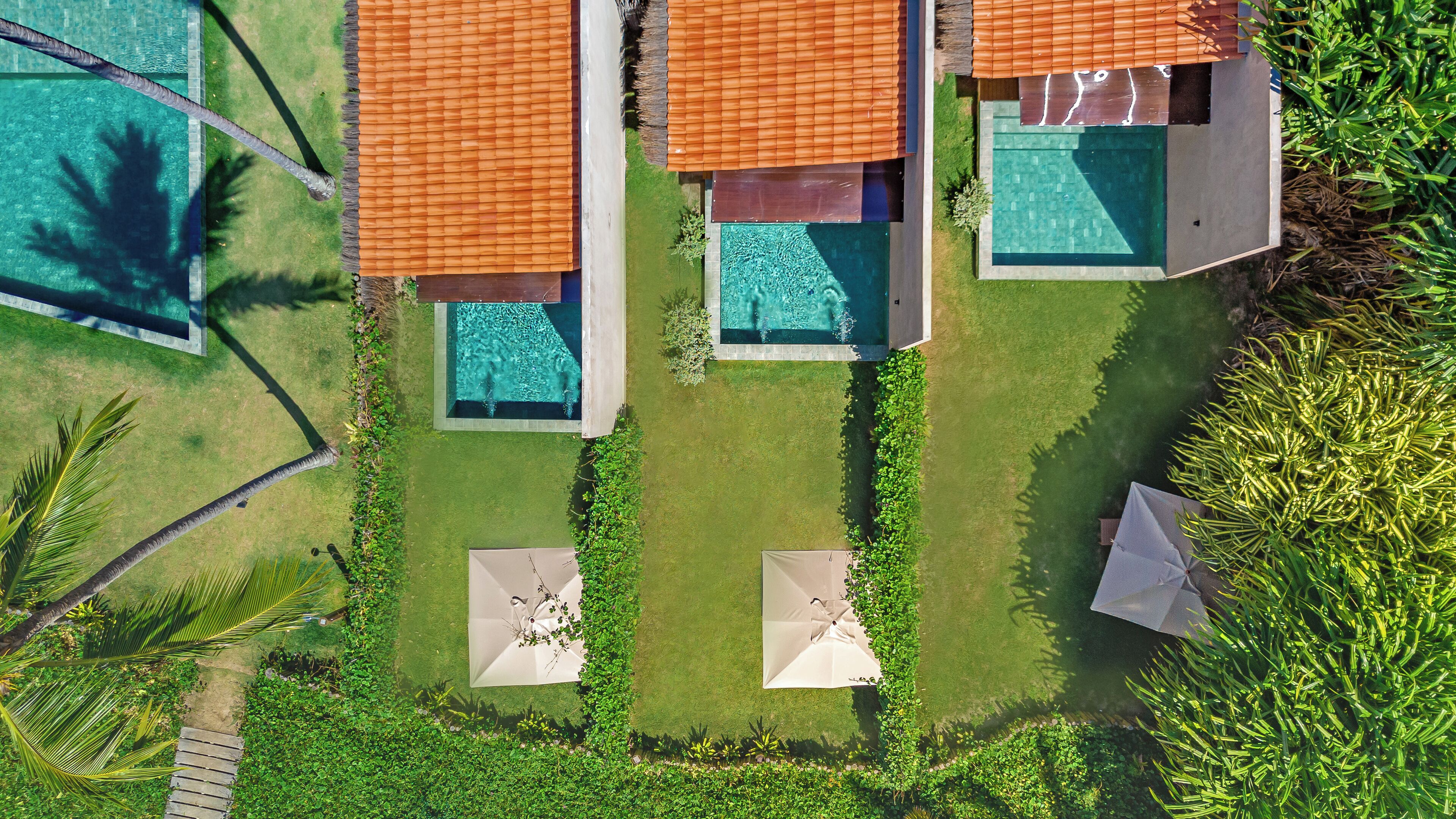 An aerial view of a resort with three separate swimming pools, each with a distinct shape and surrounded by lush greenery.