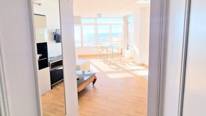 A spacious room with a large mirror, a dining area with chairs, and a view through the window.